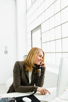 Germany, Businesswoman talking on telephone and using computer, smiling
