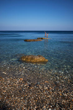 Two eight year old girls (identical twins) jump into the sea off a rock in the Greek island of Ikaria