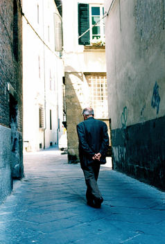 Senior Man Walking On European City Street With Hands Behind Back, Rear View.