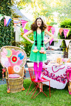 A teen girl in a colorful outfit stands on a chair yelling.