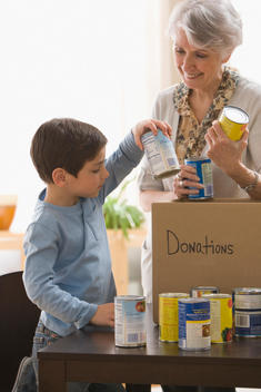 Caucasian grandmother and grandson filling box with canned goods for charity