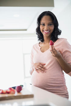 Portrait of pregnant woman eating strawberries in kitchen