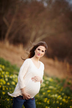 Pregnant woman holding her belly as she stands in a field in the afternoon.