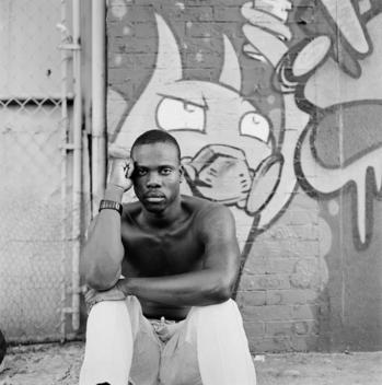 A portrait of black African-American actor Rhett George, who is in the touring Broadway musical Memphis, sitting shirtless with no top exposing chest against a wall of graffiti on an inner-city street in Bed-Stuy, Brooklyn, New York.