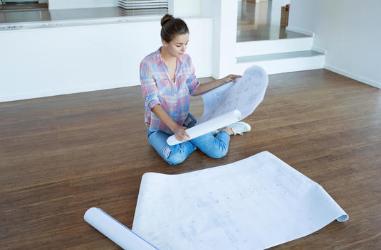 Woman examining blueprints on floor in empty living room