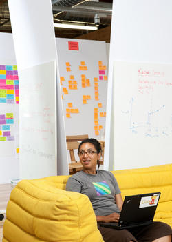 A female Google employee lounges on a yellow sofa with a laptop open