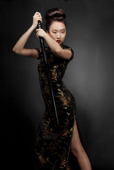 Studio beauty cropped portrait of an Asian female model holding a sword case in fighting position wearing a Japanese dress on a dark background