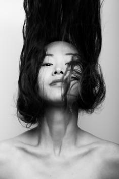 Moody shot of a young Japanese woman flicking her hair up in a swing of the head.