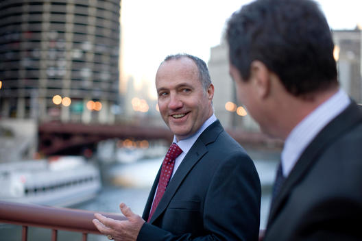 Two Business Men Walk And Talk Over A Bridge On The Chicago River.