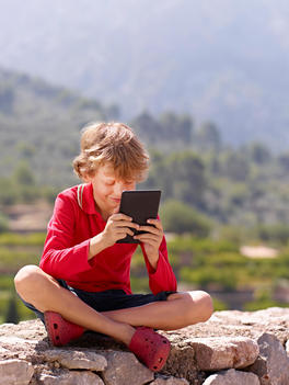 Boy sitting on stone wall looking at digital tablet, Majorca, Spain