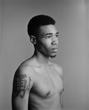Classic black and white studio portrait of Moses, a young semi-nude black, African-American guy with Japanese-character shoulder tattoo. Brooklyn, NYC
