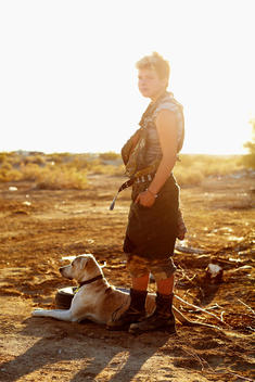 Young Woman In Camouflage And Military Boots With Dog In Sunset In Slab City, Ca.
