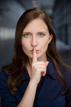 Portrait of serious young businesswoman with finger on lips in office