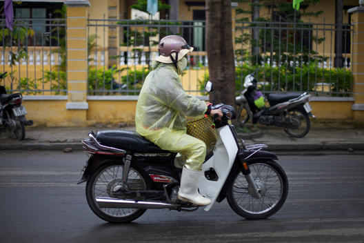 Vietnamese moped rider in yellow waterproof mac in the rain in Hoi An, Vietnam