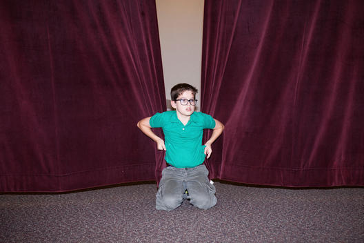 A pre-teen boy playing on a stage with his cousins holds the curtains closed at a Mormon LDS Church at a family gathering. Tyler, Texas