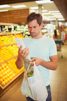 Confused man reading receipt in grocery store
