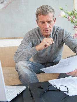 Germany, Munich, Mature man doing paperwork with laptop