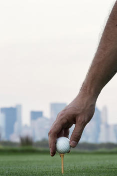 Hand holding golf ball at surface level with Manhattan in the background