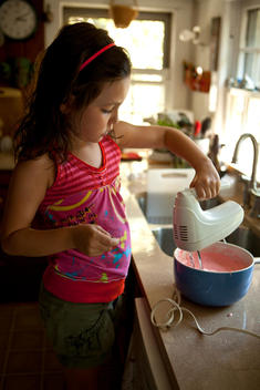 A young girl using a blender to mix pink cake batter.