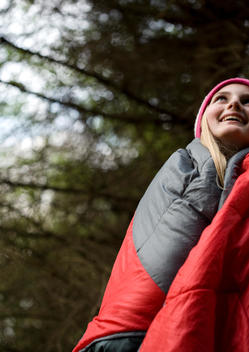 Standing teenaged girl wrapped in a sleeping bag looking up and smiling