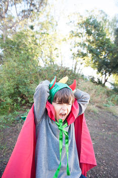 6 year old caucasian boy, brown hair, in a dragon cape costume with hands behind head and yelling.