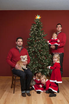 A gay couple pose for a holiday portrait with their daughters and dog.