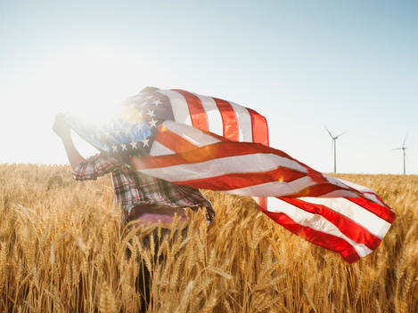 Girl (12-13) flying american flag in wheat field