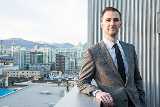 Portrait of man in suit outside with city skyline in background.