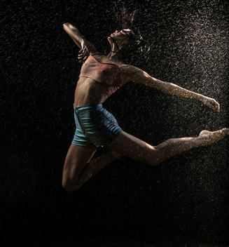 A woman dancing athletically in the rain.