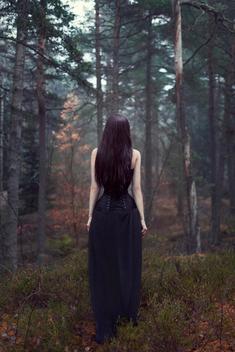 Girl with long hair wearing a corset seen from behind standing in woodland alone