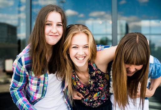 Portrait of three young women laughing in front of glass office building