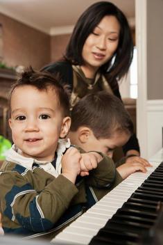 Asian mother teaching sons to play piano