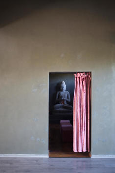 A view to statue of Buddha in a meditation room through a doorway with a pink curtain
