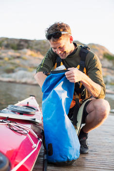 Happy man searching something in bag by kayak