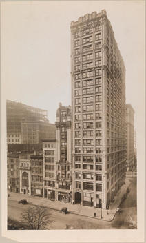 The Southwest Corner Of 5Th Avenue And 26Th Street. On The Corner Is A Tall Building, And Several Smaller Buildings Line The Street, All Housing Businesses And Stores.