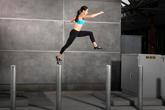 Athletic woman leaping between car poles, wearing exercise clothing