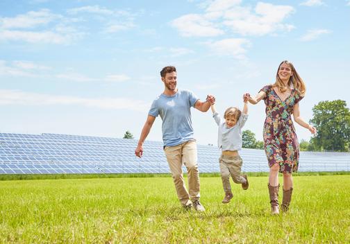 Mother and father holding hands with son, walking across field next to solar farm
