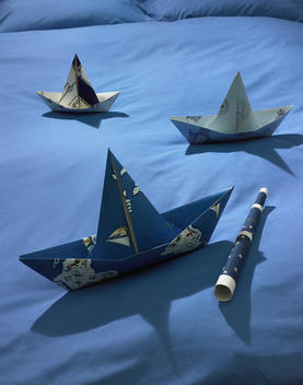 Still life of folded paper ships on a blue duvet.