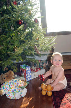 Smiling baby sitting under tree holding red bow