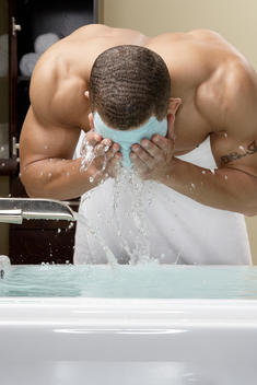 Mixed race man washing off facial mask in bath