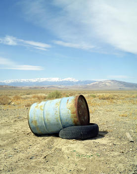 A Blue Oil Drum Laying On An Old Tire In A Desert Setting.