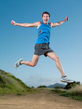 An athletic man jumps up in the middle of a hiking trail