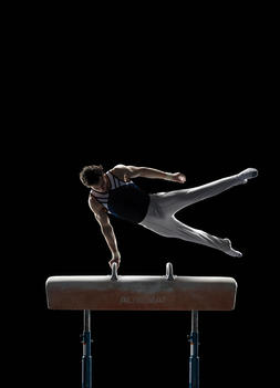 Athletic Olympic artistic gymnast performing scissor swing on pommel horse