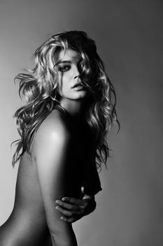 black and white image of a caucasian model in her late 20\'s with long blond curley hair, topless and looking at the camera