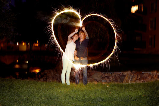 Female couple embracing creating a heart with fireworks