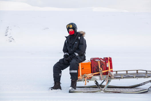 A glaciologist waits seated on a snowmobile sled in Sassendalen, Svalbard on a class field trip to Tunabreen.