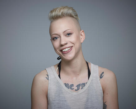 Portrait of young woman with tattoos against grey background, smiling