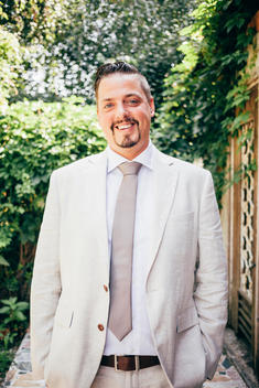 thirty something man with goatee and dark hair in white suit with tie laughing.