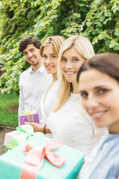 Portrait of young man and three women holding birthday gifts in garden