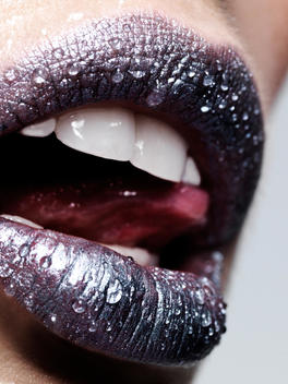 Water droplets on young woman in purple lipstick, close up